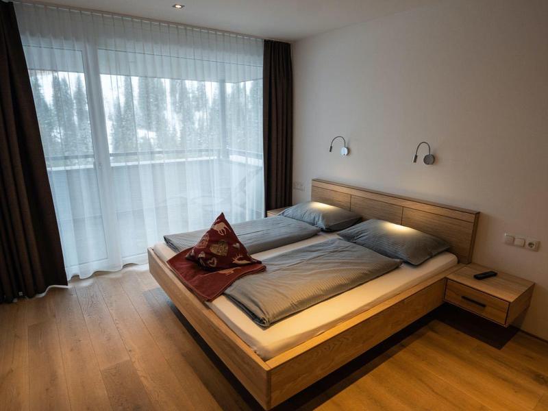 Modern hotel room with double bed, wooden floor, and large window with curtains.