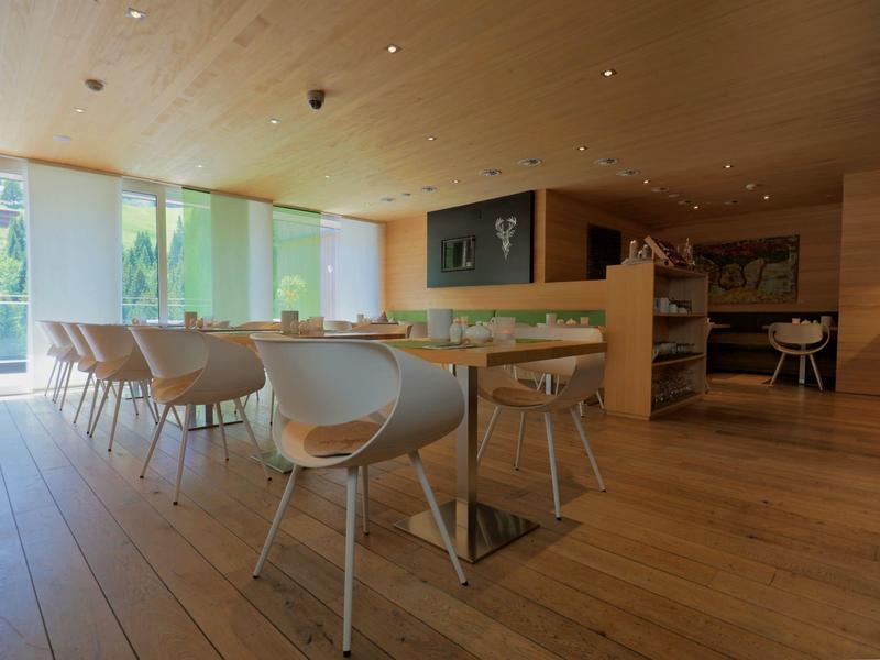 Modern dining area with wooden floor, white chairs, and large windows with green curtains.