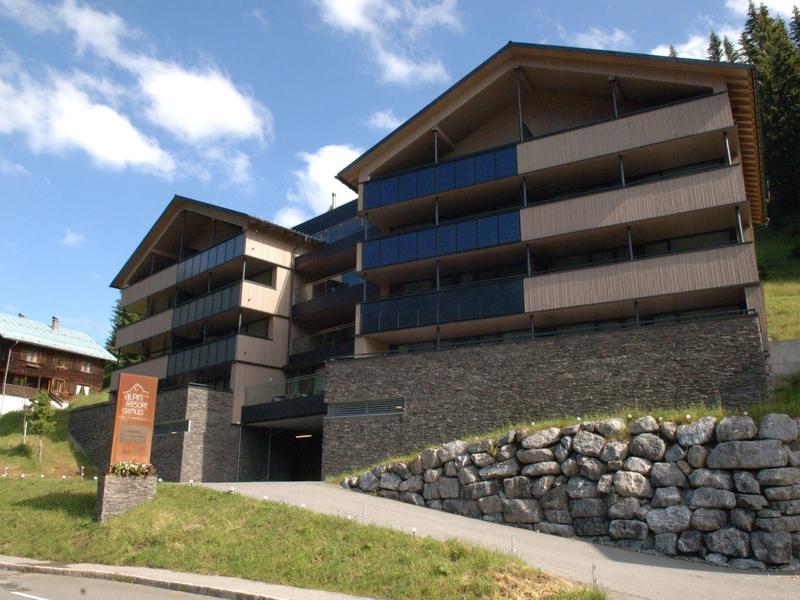 Modern hotel building with large balconies on a hillside and green grass below.