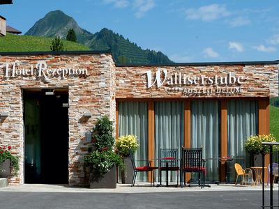 Moderner Empfangsbereich mit heller Steinfassade, großen Fenstern, Tischen und Bergen im Hintergrund.