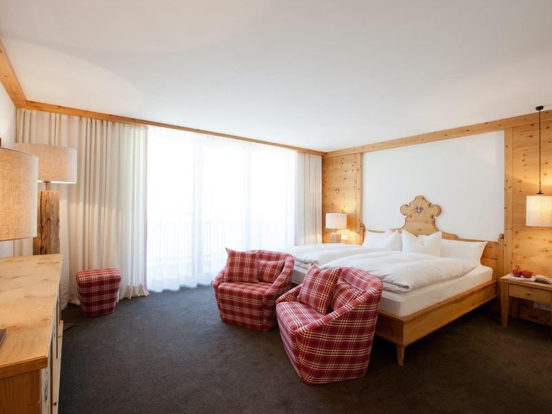 Cozy hotel room with wooden walls, double bed, and plaid armchairs in daylight.