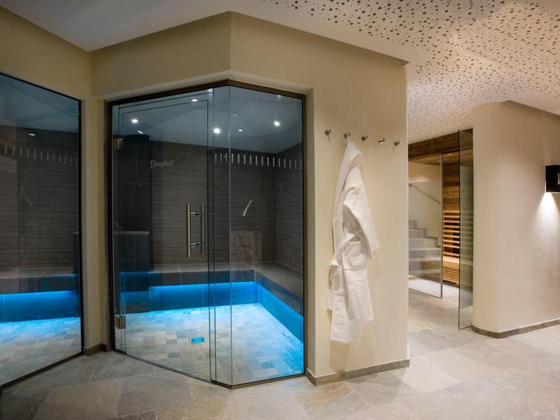 Modern spa area with sauna and illuminated hot tub under bright ceiling lights.