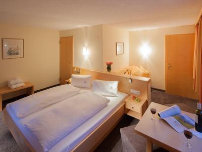 Gezellige hotelkamer met tweepersoonsbed, tafel, stoelen en warme verlichting.