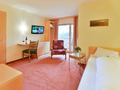 Lichte hotelkamer met eenpersoonsbed, bureau, fauteuil en groot raam met uitzicht op balkon.