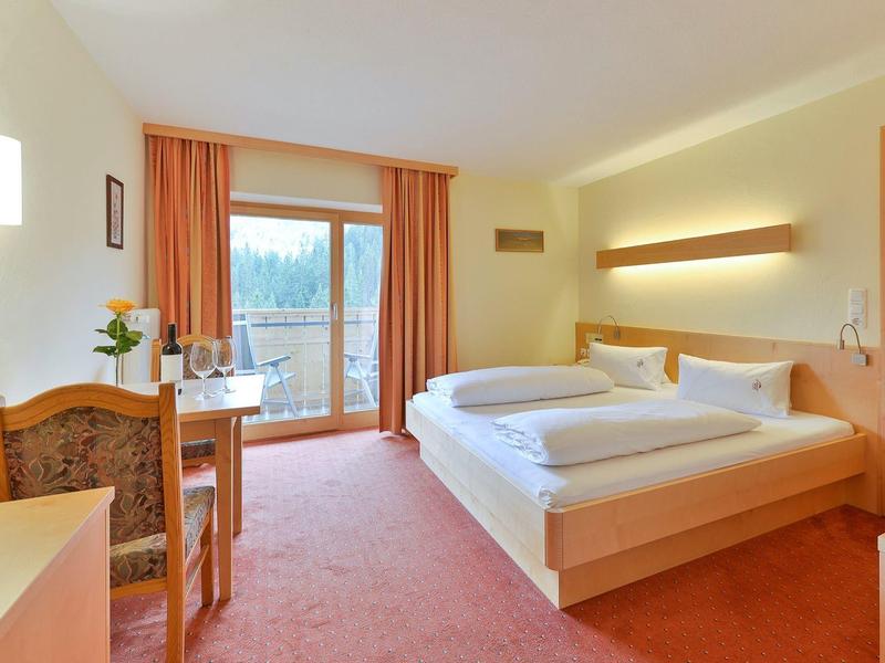 Licht ingericht hotelkamer met tweepersoonsbed, bureau en balkon met uitzicht.