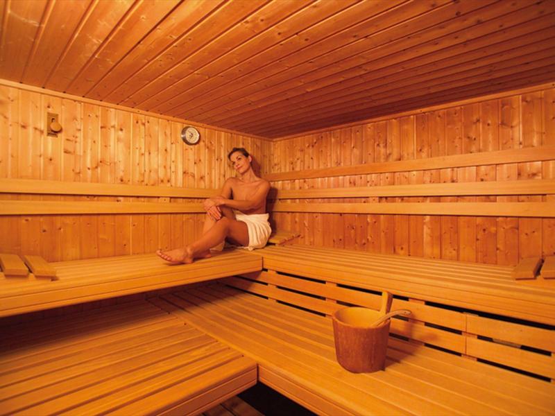 Een man zit ontspannen in een traditionele houten sauna met emmer en pollepel.