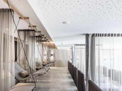 Moderner Raum mit Hängebetten, sanfter Beleuchtung und großen Fenstern mit weißen Vorhängen.