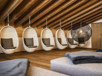 Raum mit Holzdecke, fünf weißen Hängesesseln und einem schwarzen Netzsessel, Holzboden, Kissen.