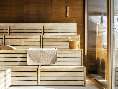 Innenraum einer Sauna mit hellem Holz, Holzbänken und einem Eimer mit Schöpfkelle.