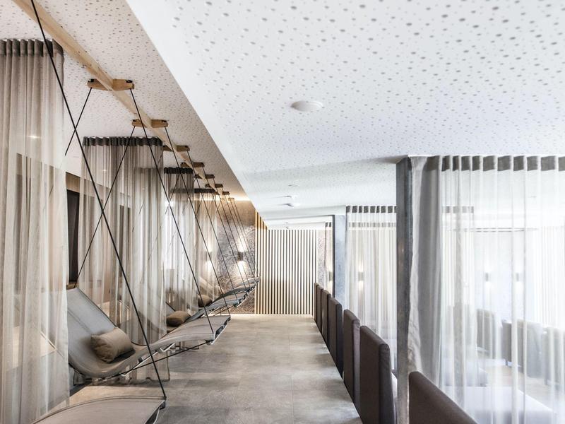 Moderner Raum mit Hängebetten, sanfter Beleuchtung und großen Fenstern mit weißen Vorhängen.