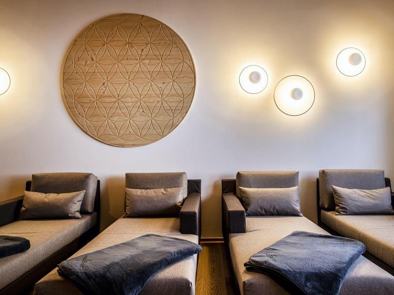 Vier moderne Sessel mit Kissen, Wandlampen und eine große runde Wanddekoration aus Holz.