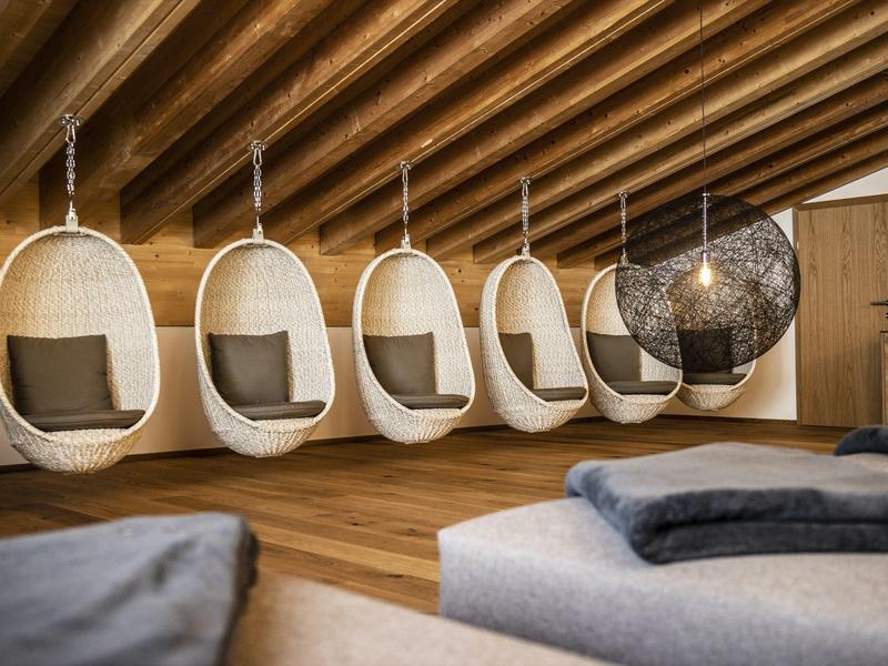 Raum mit Holzdecke, fünf weißen Hängesesseln und einem schwarzen Netzsessel, Holzboden, Kissen.