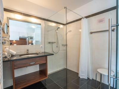 Salle de bain moderne avec grande douche, lavabo et tabouret.