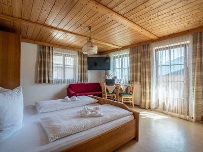 Chambre d'hôtel confortable avec lit en bois, canapé, chaises et beaucoup de lumière naturelle.