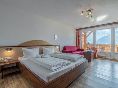 Chambre d'hôtel lumineuse avec lit double, canapé et vue sur la montagne depuis le balcon.