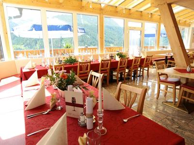 Restaurant lumineux avec nappes rouges, décorations et vue sur la montagne à travers de grandes fenêtres.
