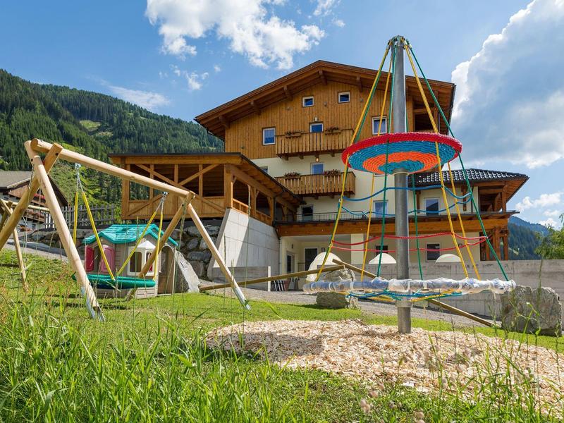 Dřevěný dům s hřištěm a kolotočem v horách za slunečného dne.