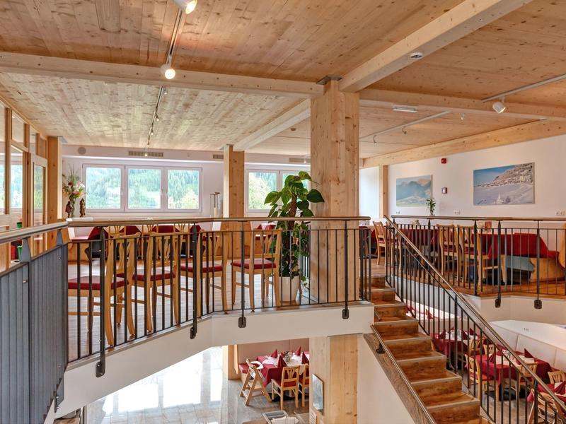 Světelná dvoupodlažní restaurace s dřevěným nábytkem a velkými okny s výhledem.