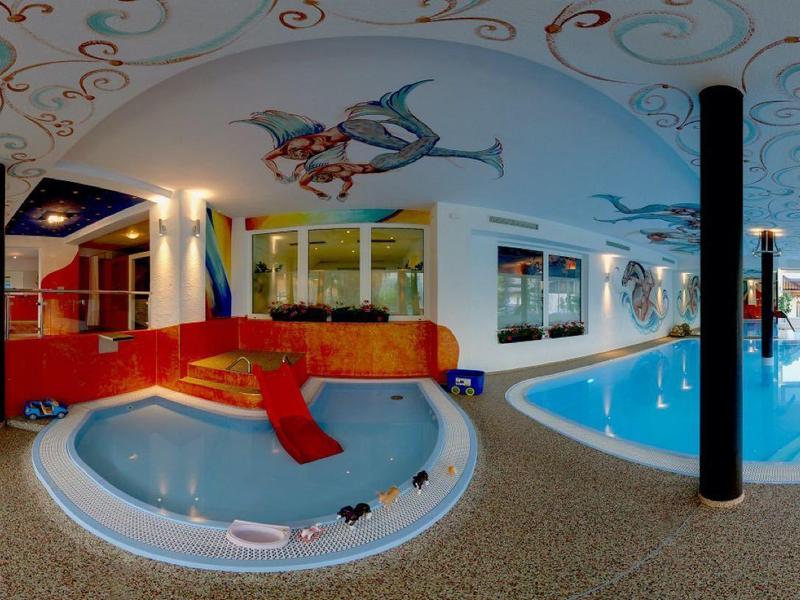 Interiér wellness se zahradní vířivkou, bazénem a dekoracemi na strope a stěnách.