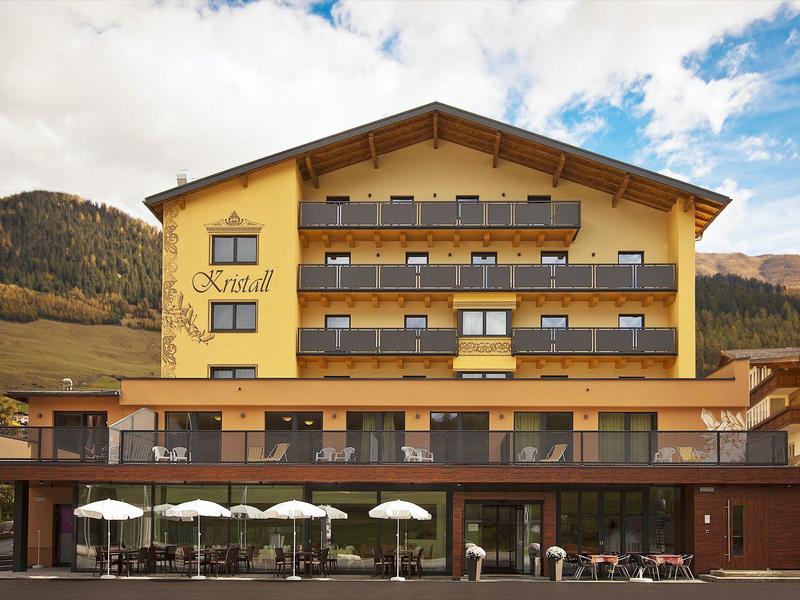 Nowoczesny żółty budynek hotelu z balkonami na tle górskiego krajobrazu w świetle dziennym.