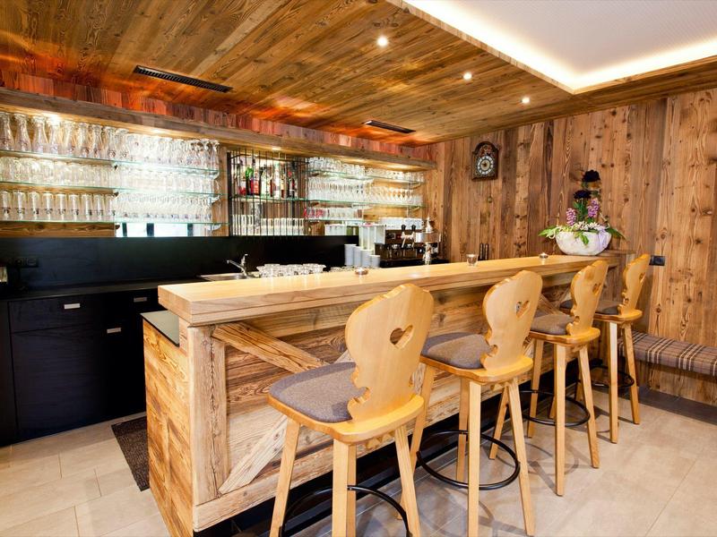 Drewniany bar z wysokimi stołkami i tłem z kieliszkami oraz drewnianą boazerią.