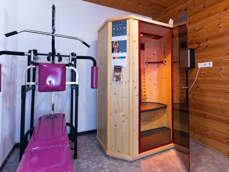 Mała siłownia z urządzeniem do ćwiczeń siłowych i drewnianą sauną w pomieszczeniu z drewnianą ścianą.