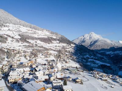 Pueblo nevado con casas en un valle montañoso bajo un cielo azul claro.