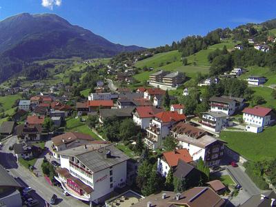 Pueblo de montaña con casas, praderas verdes y montañas bajo un cielo azul claro.