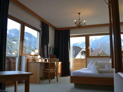 Habitación de hotel luminosa con grandes ventanas, muebles de madera, cama y escritorio, vista a las montañas.