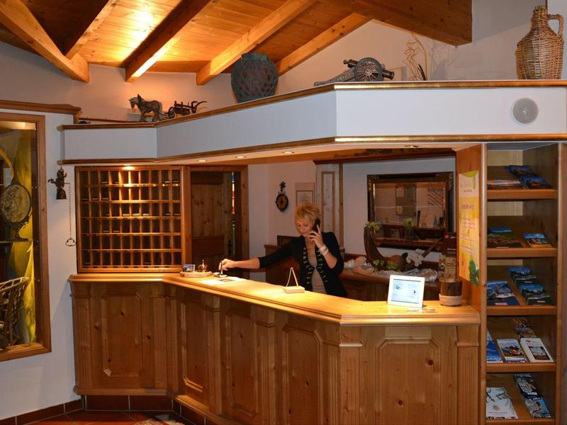 Recepción de hotel con mostrador de madera y una persona atendiendo bajo techo con vigas visibles.