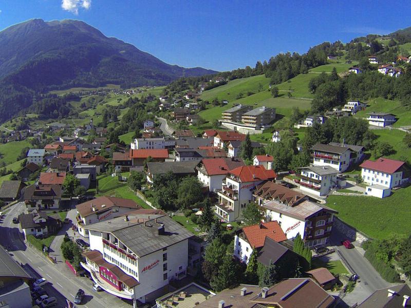 Pueblo de montaña con casas, praderas verdes y montañas bajo un cielo azul claro.
