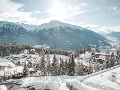 Snow-covered mountain landscape with village and fir trees under blue sky with clouds.