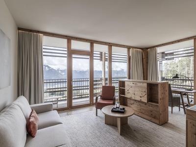 Cozy living room with sofa, wooden windows, and mountain view in daylight.