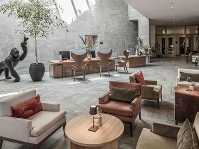 Modern hotel lounge area with comfortable armchairs, tables, and decorative sculpture.