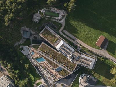 Aerial view of a modern hotel with green roofs surrounded by forest and meadows.