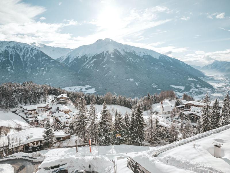 Snow-covered mountain landscape with village and fir trees under blue sky with clouds.