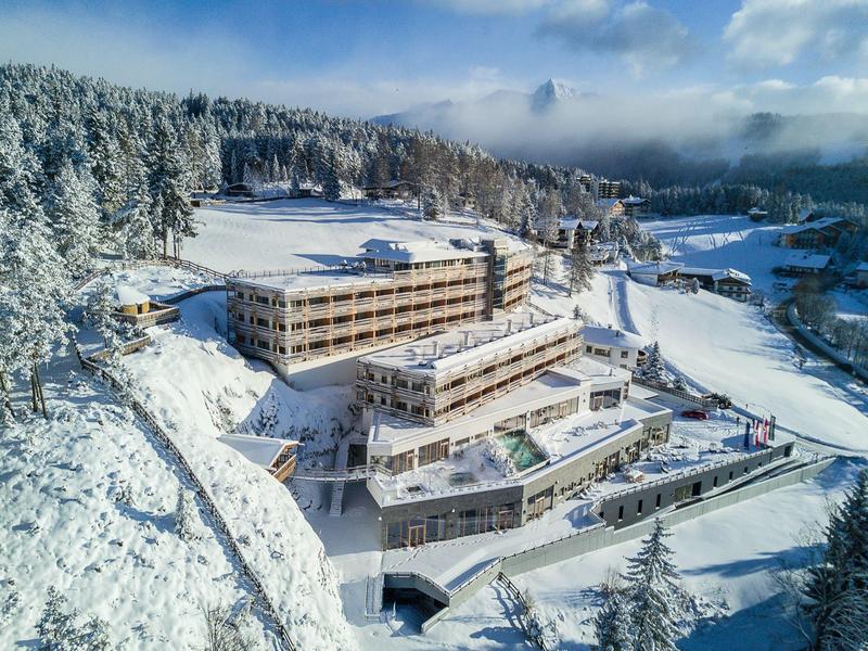 Large hotel in snowy mountain landscape with pine trees and cloudy sky.