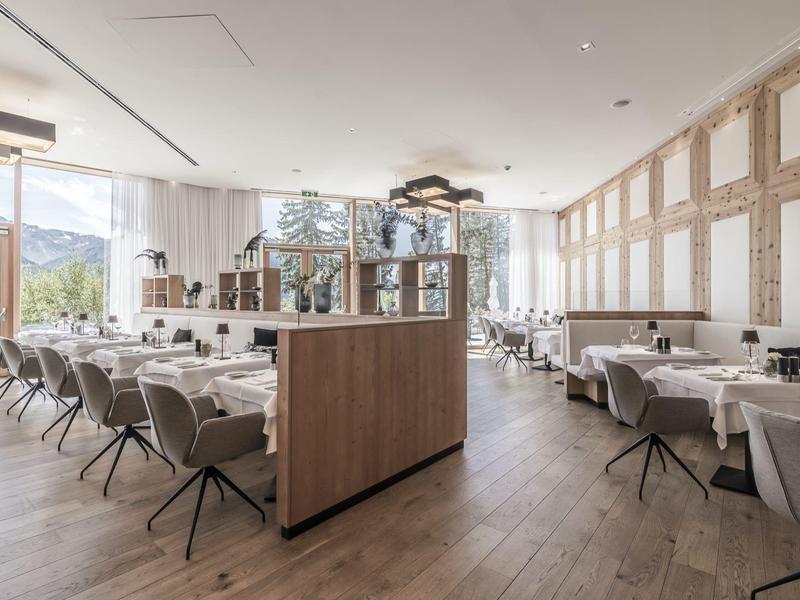 Modern bright restaurant with wooden floor, many tables, and gray chairs.
