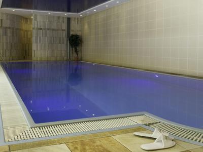 Kryty basen z jasną, kafelkowaną powierzchnią i białymi kapciami przy krawędzi