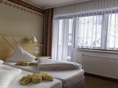 Przytulny pokój hotelowy z dwoma pojedynczymi łóżkami, dużymi oknami i zasłonami.