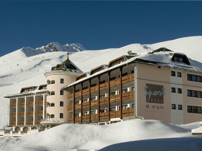 Budynek hotelu z drewnianą elewacją w zaśnieżonym górskim krajobrazie pod błękitnym niebem.