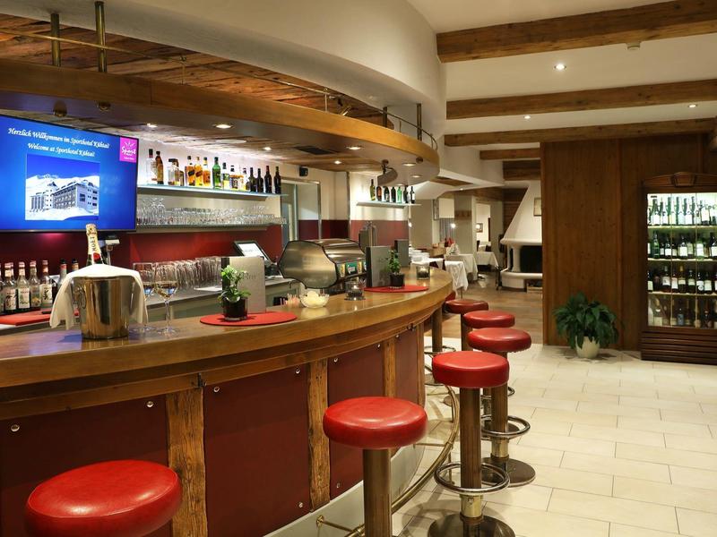 Przytulny bar hotelowy z drewnianym kontuar, czerwonymi stołkami i telewizorem na ścianie.