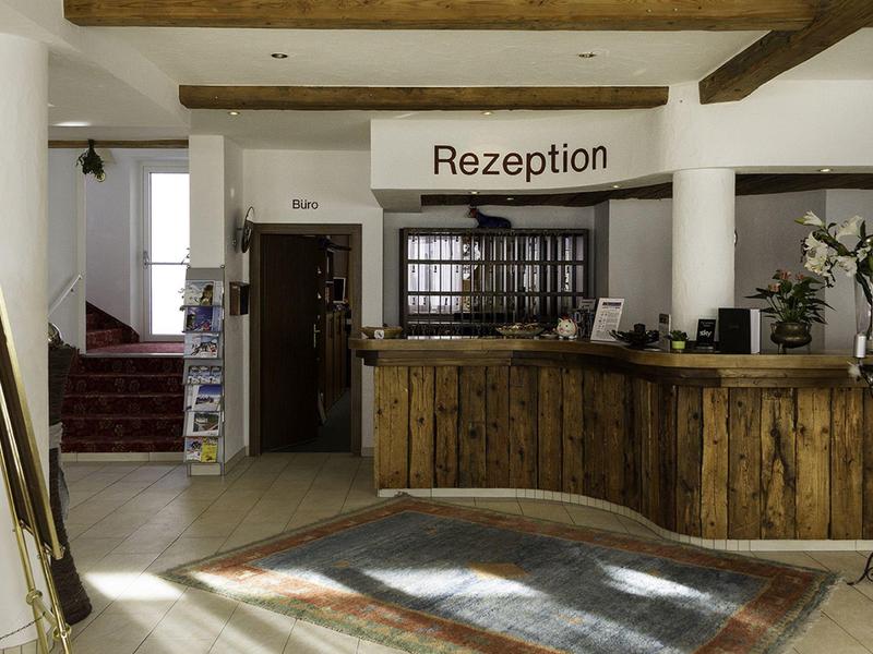 Rustykalna recepcja hotelowa z drewnianym kontuarem i tabliczką 'Recepcja' w ciepło oświetlonym wejściu.