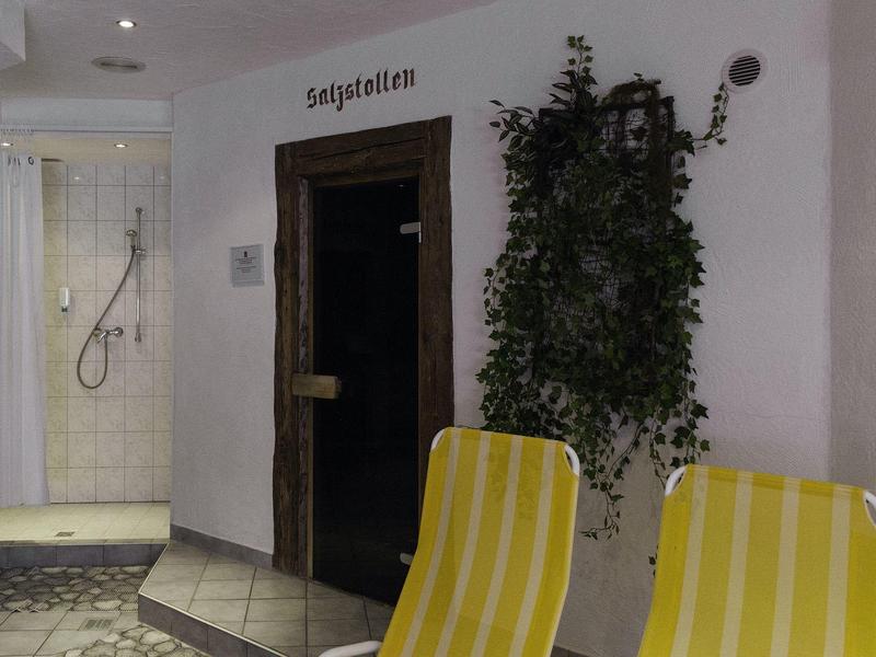 Mały obszar sauny z drewnianymi drzwiami, kabiną prysznicową i żółtymi leżakami.