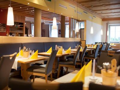 Elegancka restauracja z drewnianymi stołami, szarymi krzesłami i żółtymi serwetkami w ciepło oświetlonym pomieszczeniu.