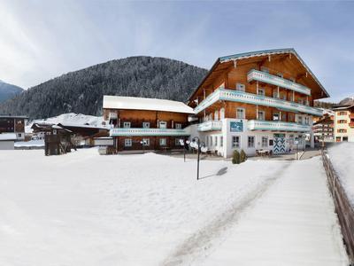 Schneebedeckte Landschaft mit Holzhäusern und Bergen im Hintergrund unter blauem Himmel.