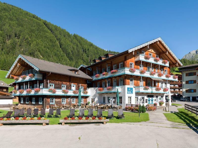 Tradiční alpský hotel s květinovou výzdobou, obklopený zelenými horami pod jasnou oblohou.