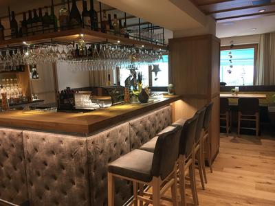 Area bar moderna in hotel con bancone imbottito e sgabelli in legno e tessuto