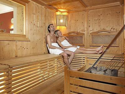 Coppia che si rilassa in una sauna di legno accogliente, entrambi con asciugamani bianchi.