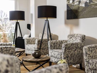 Soggiorno luminoso con poltrone a motivi e due lampade da terra nere su pavimento in legno.